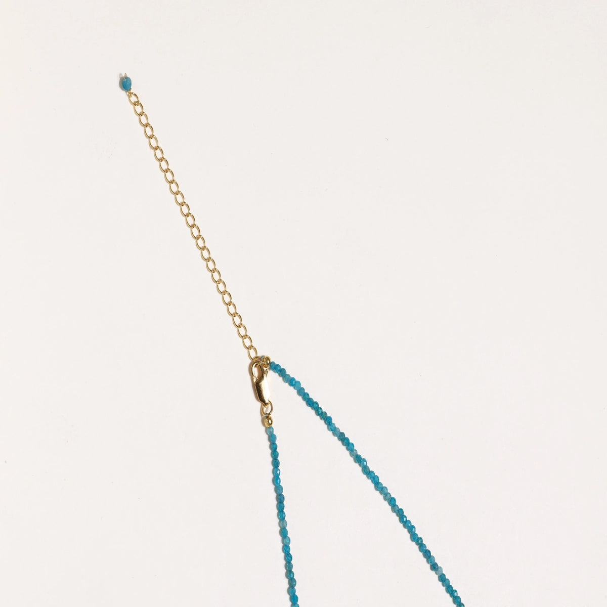 Delicate gold vermeil necklace with teal apatite beads and freshwater pearl on white background.