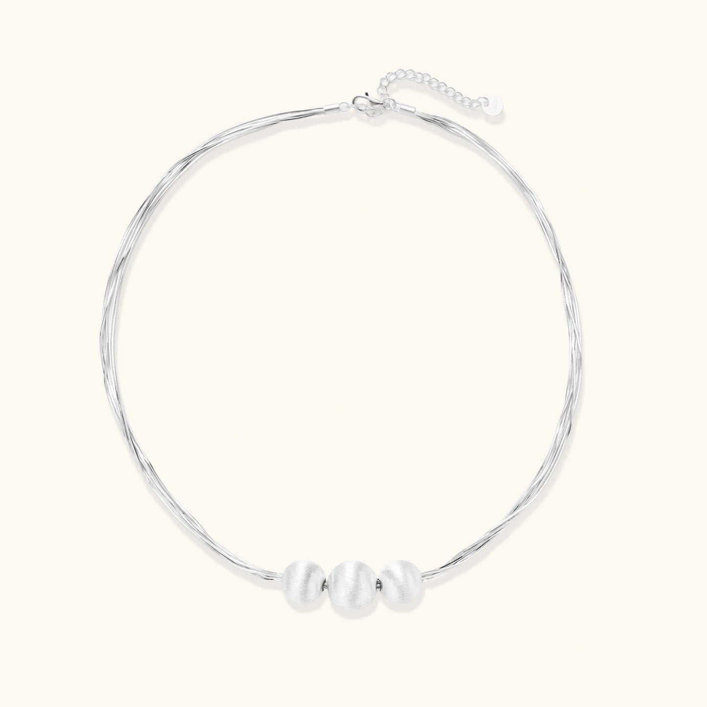 Sterling silver multi-strand necklace with three brushed round beads on cream background