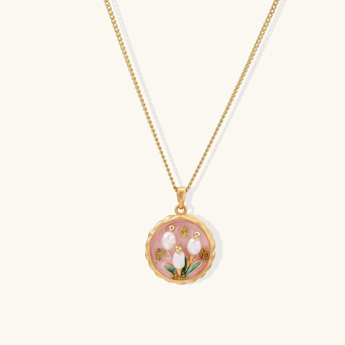 Gold pendant with pink enamel backdrop, white freshwater pearls as tulip blooms, and green leaf accents on rope chain.